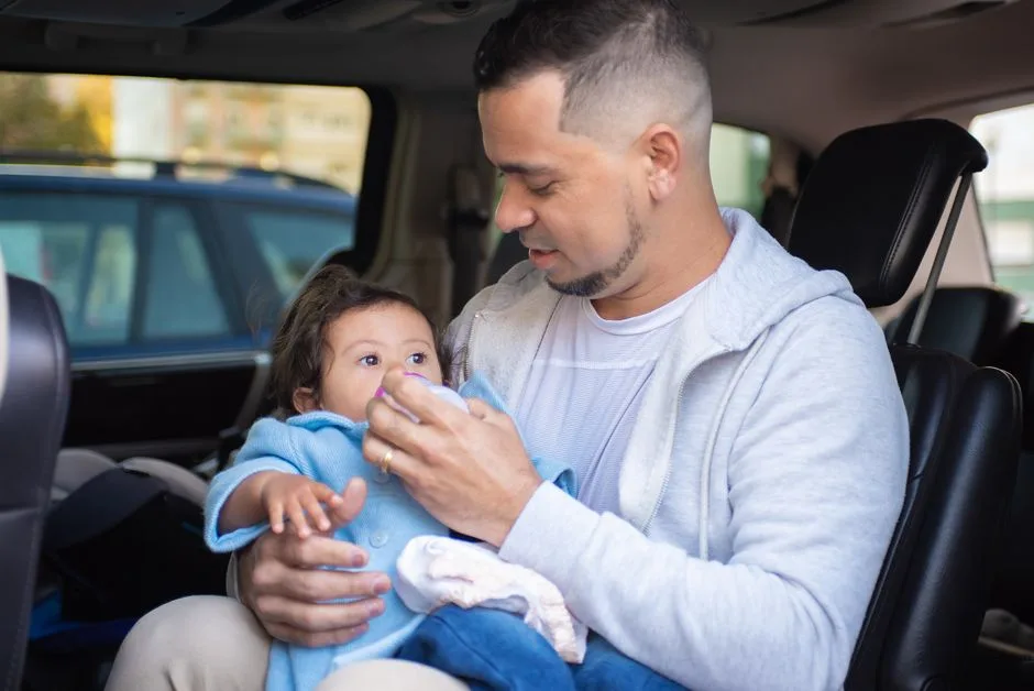 한 남성이 자동차 내부 좌석에 앉아 어린아이를 안고 얼굴을 닦아주거나 돌보는 모습이다. 배경에 다른 차량이 보이지만 로고, 상표, 브랜드 식별 문구, 워터마크, 가격, 프로모션, 전자상거래 UI 또는 리뷰 화면은 보이지 않는다.
