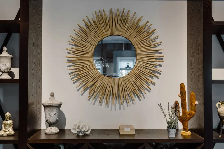 A sunburst-framed round mirror hangs above a console table decorated with urns, sculptures, a small plant, and other ornaments; no person is visible.