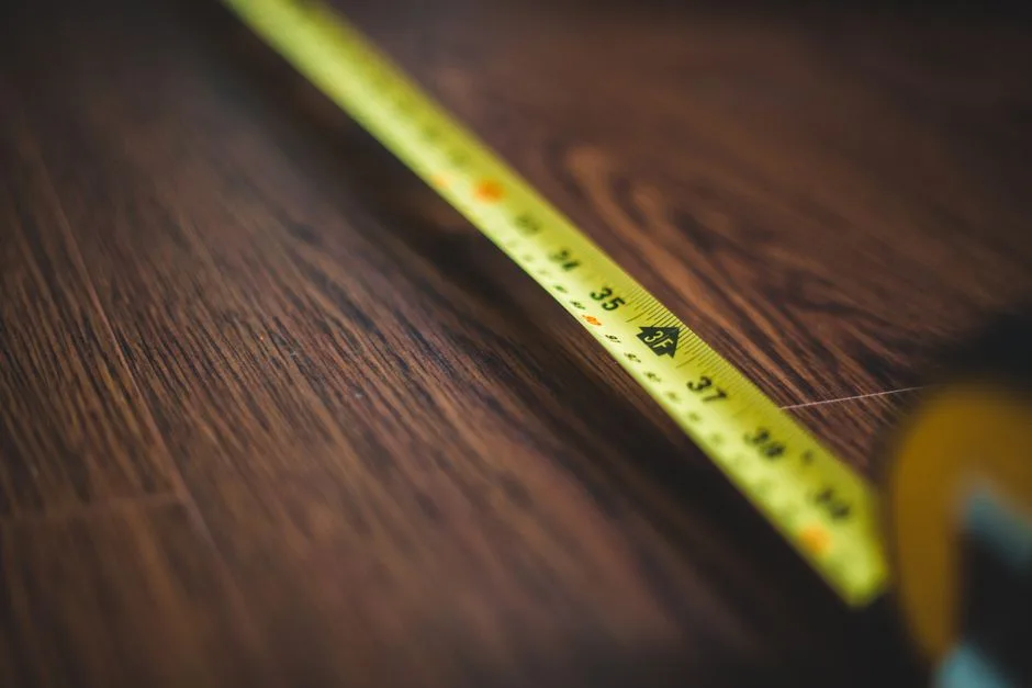 A close-up of a generic yellow measuring tape extended diagonally across a dark wooden surface; no person, hand, kitchen counter, or installation space is visible.