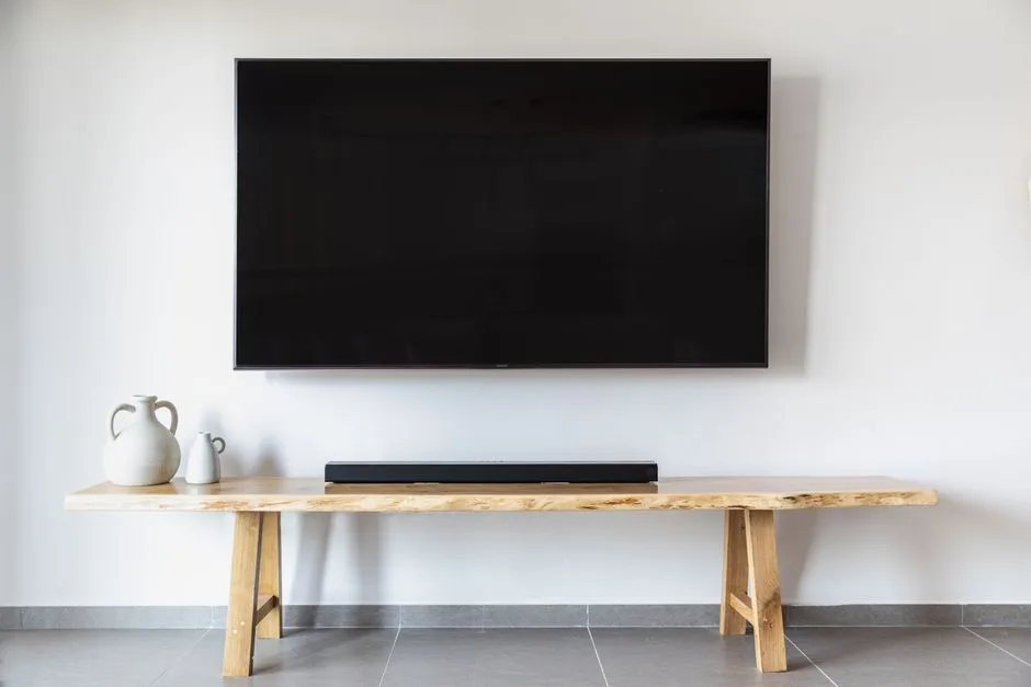 A wall-mounted television above a rustic wooden bench or console table, with a soundbar and two decorative ceramic vessels. No visible branding, logos, text, watermark, pricing, promotion, ecommerce UI, product listing, or review content.