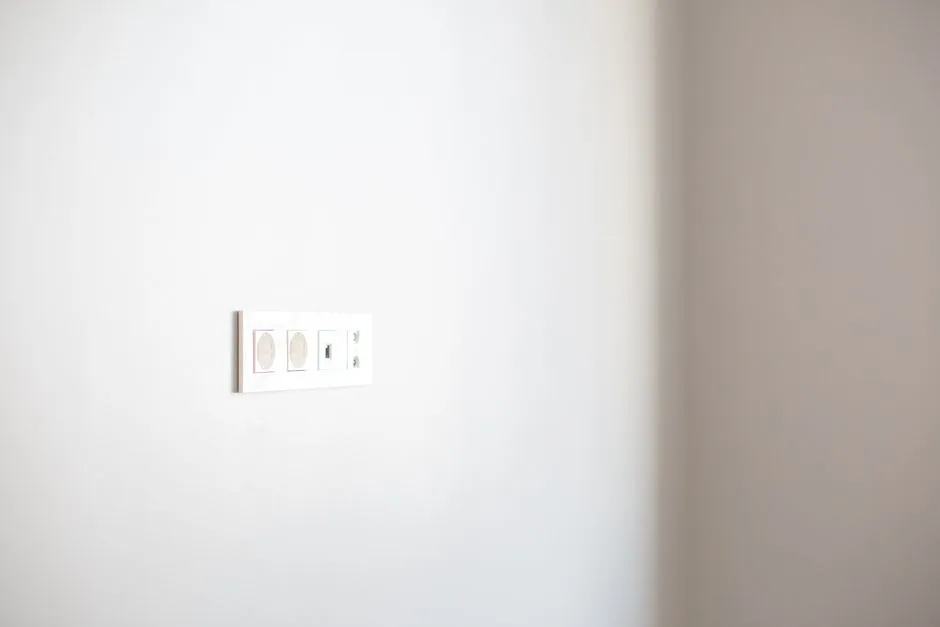 밝은 실내의 흰색 벽과 벽면 콘센트·스위치 패널이 보이며, 청소용품이나 가구는 보이지 않습니다.