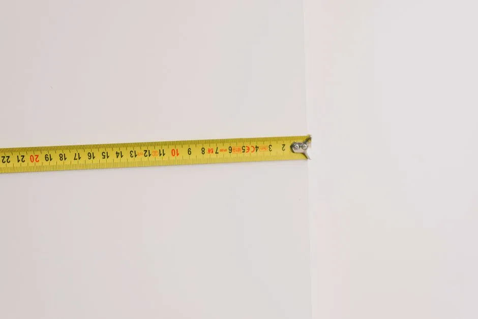 흰색의 평평한 표면 위에 노란색 줄자가 펼쳐져 있으며, 세탁 바구니나 뚜렷한 세탁 공간은 보이지 않는다.