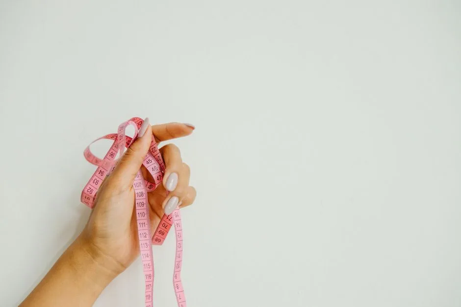 A hand holds a pink measuring tape against a plain light-colored background; no kitchen or storage cabinet is visible.